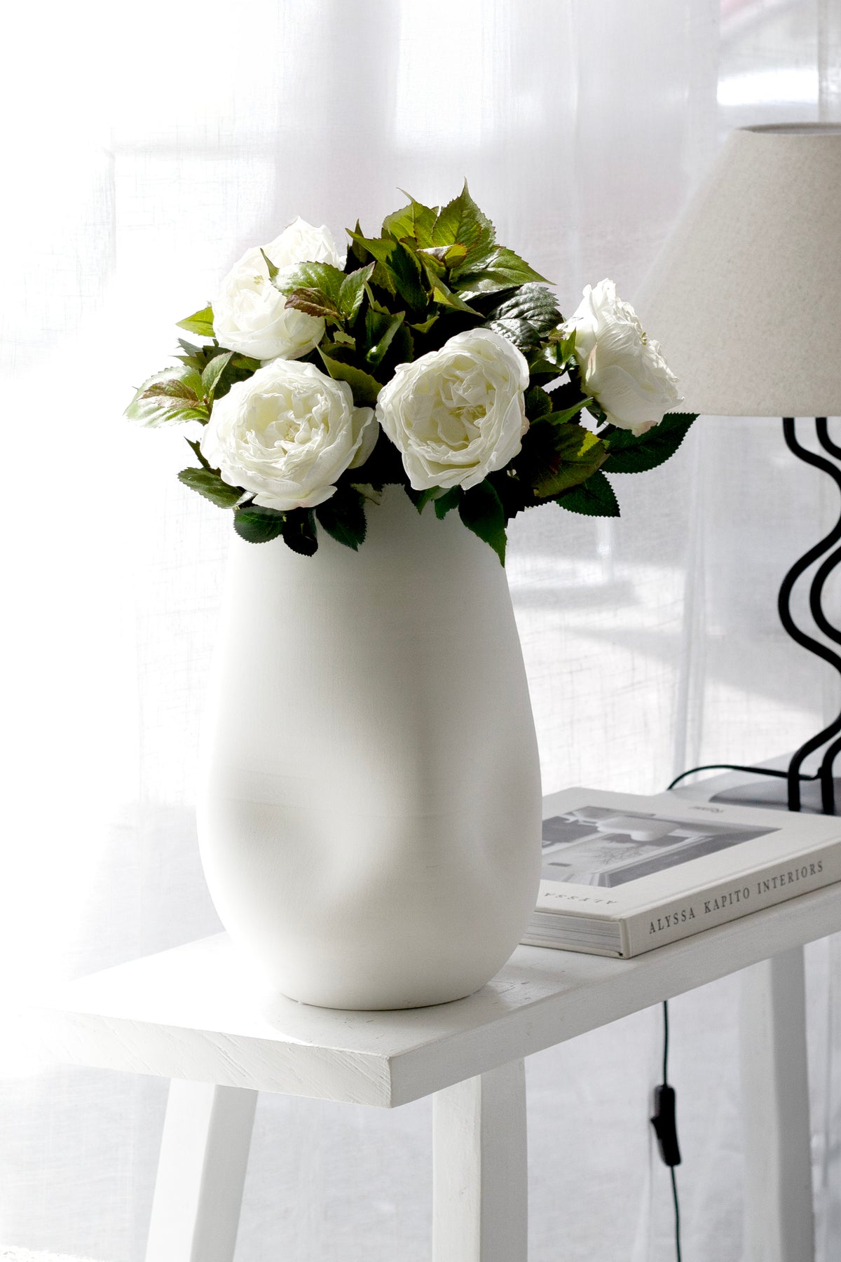 Ivory Austin roses styled on a white console with a lamp and stacked books