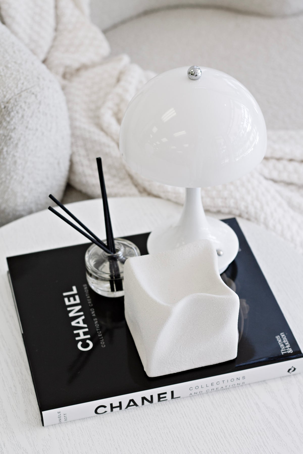 White Cubic Crush cube on stacked books beside a domed lamp, seen from further back