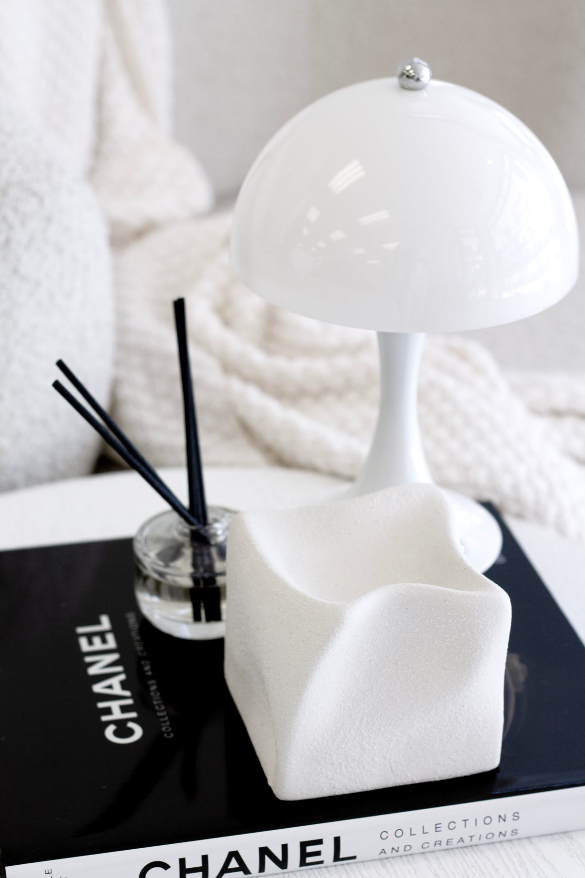 White Cubic Crush cube on stacked books with a domed lamp and a reed diffuser behind