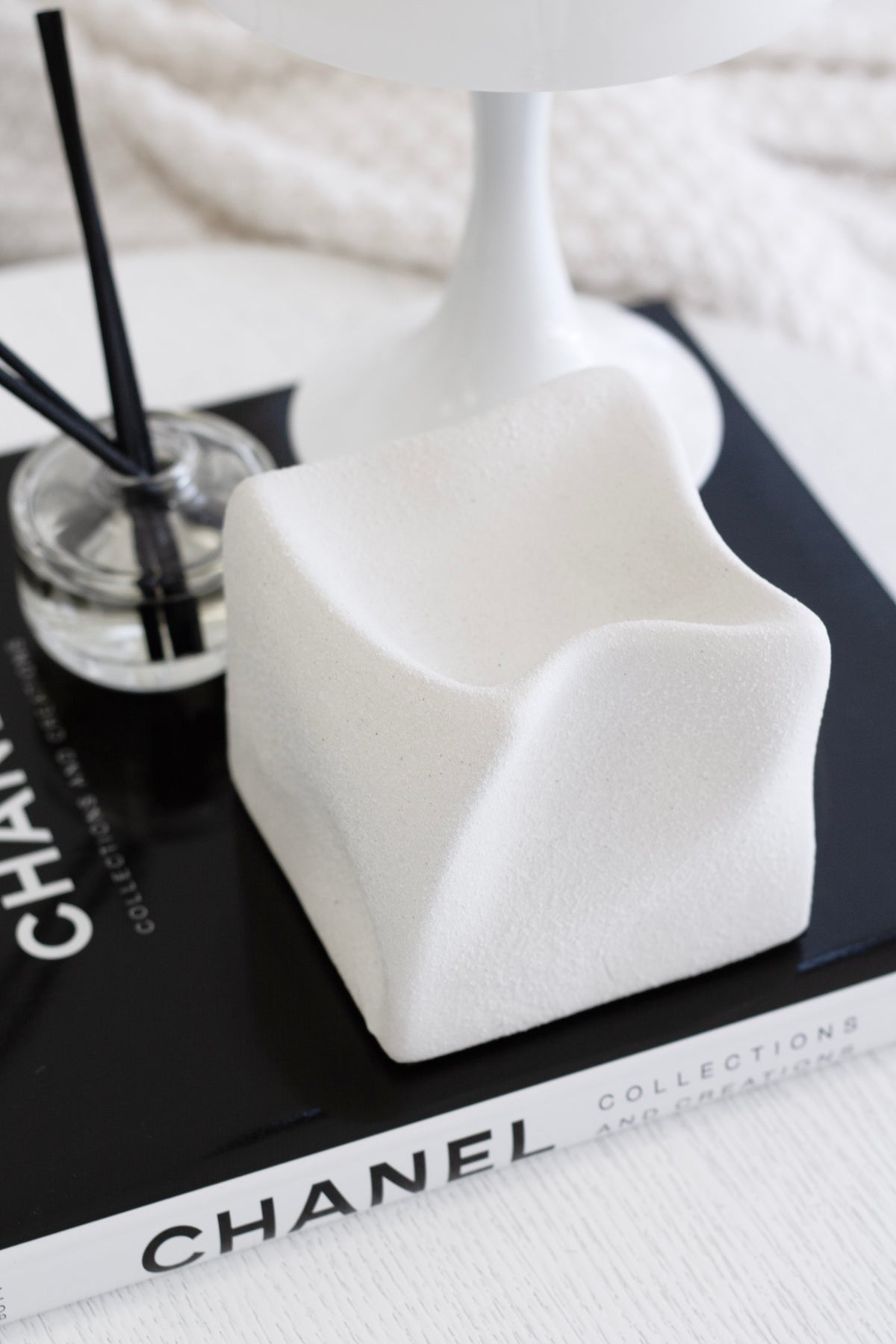 White Cubic Crush cube on a book beside a lamp base and a reed diffuser