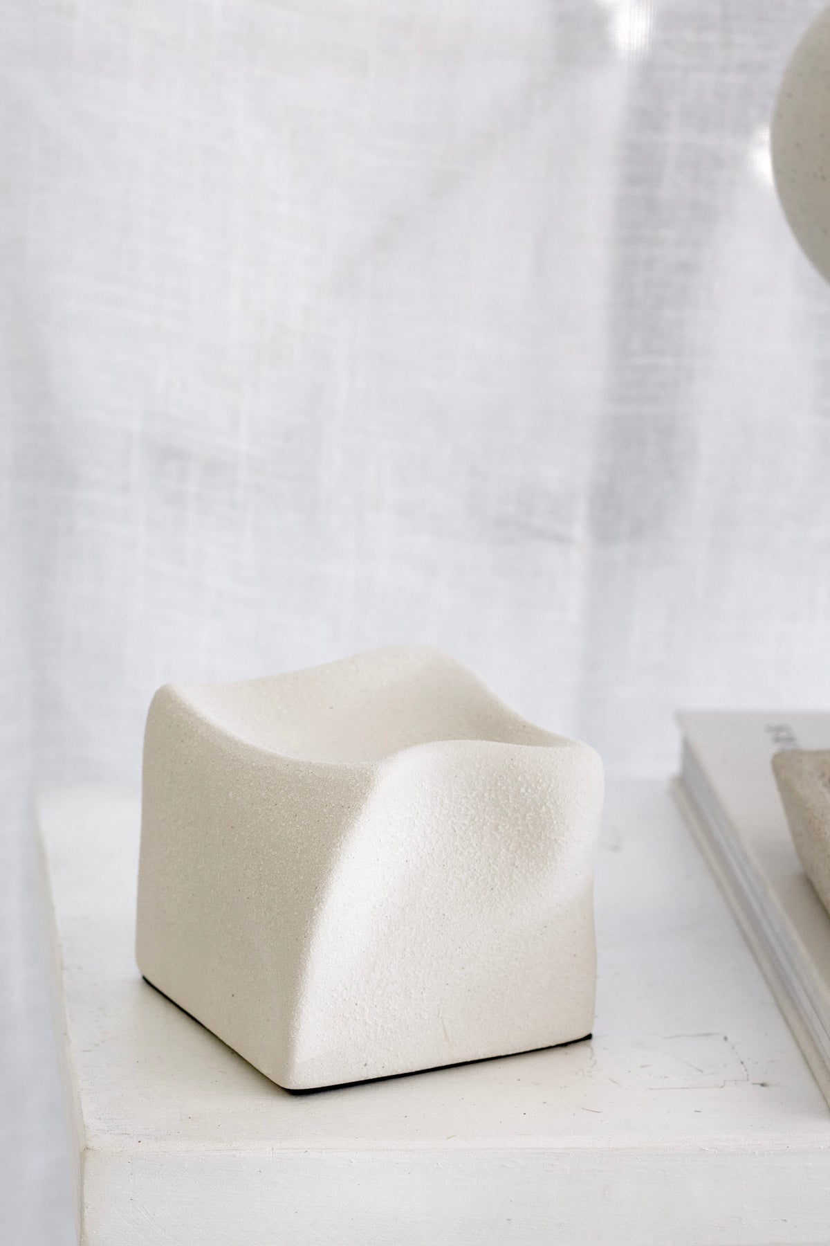 White Cubic Crush cube on a plinth with a sheer curtain behind
