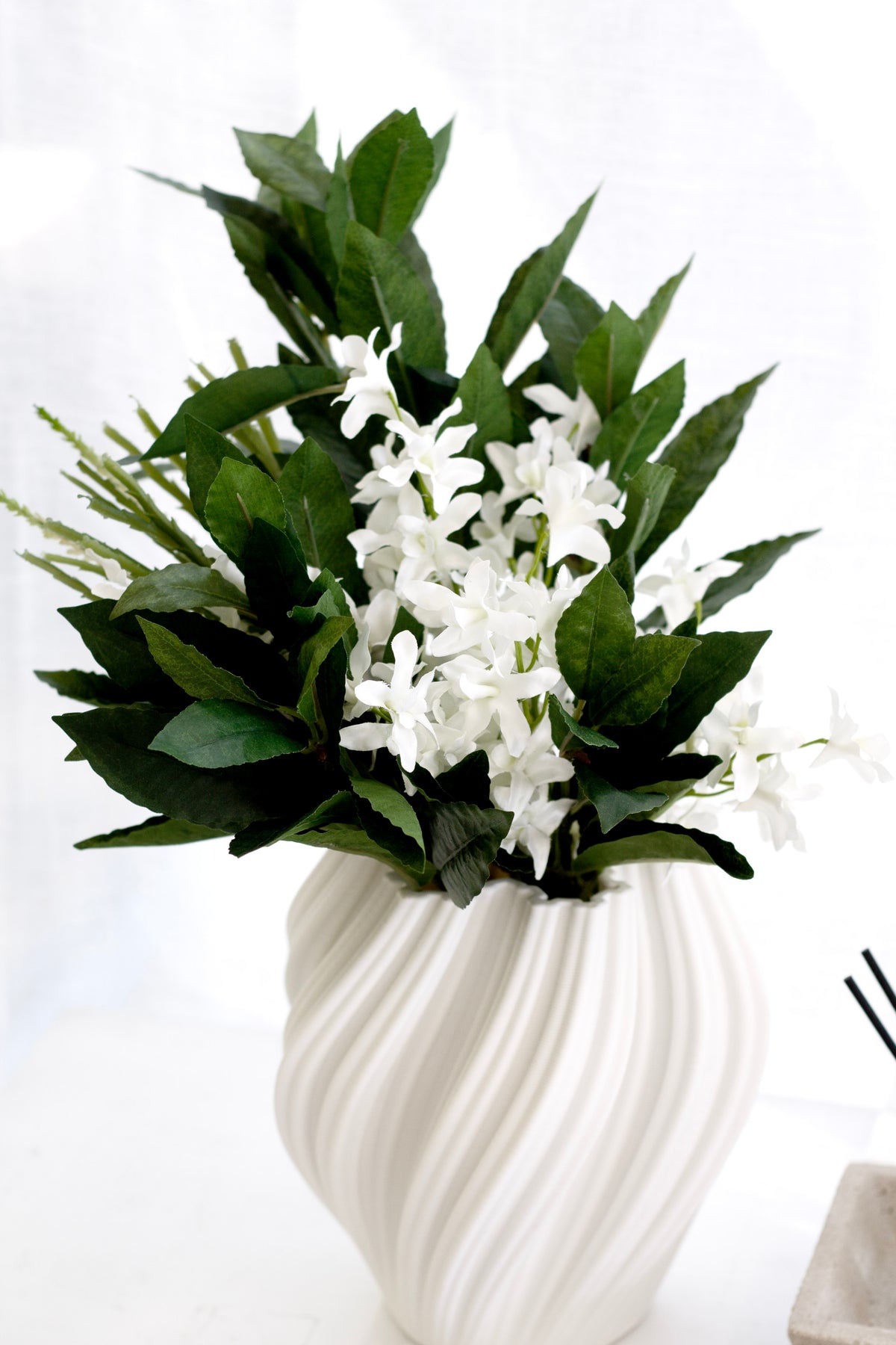 Faux orchids with green leaves in a white swirl vase