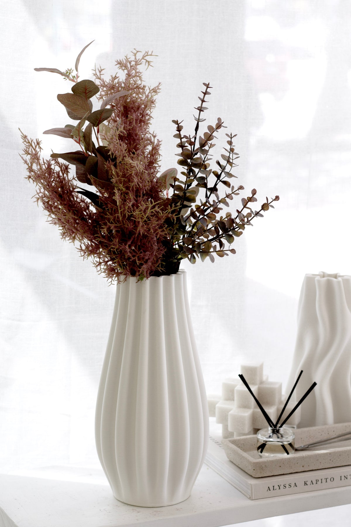 Grey-pink eucalyptus with dried stems in a ribbed cream vase beside a wick trimmer