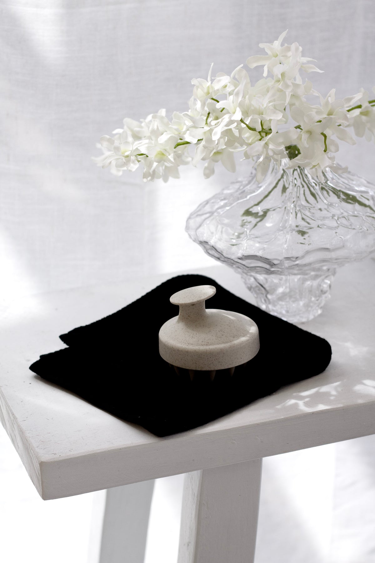 Black wash cloth under a white brush on a white stool beside a glass vase of orchids