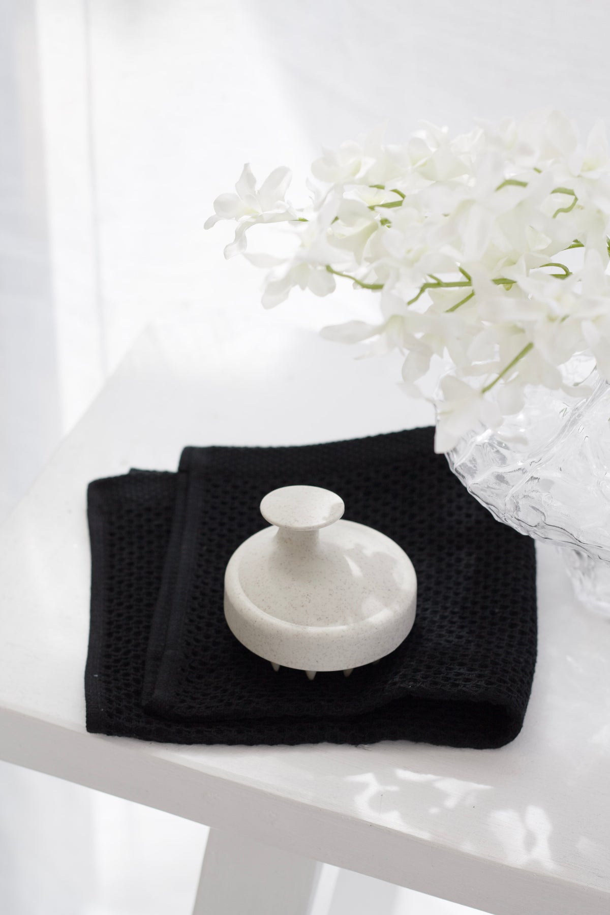 Black cotton wash cloths on a white stool with a white brush and white orchids