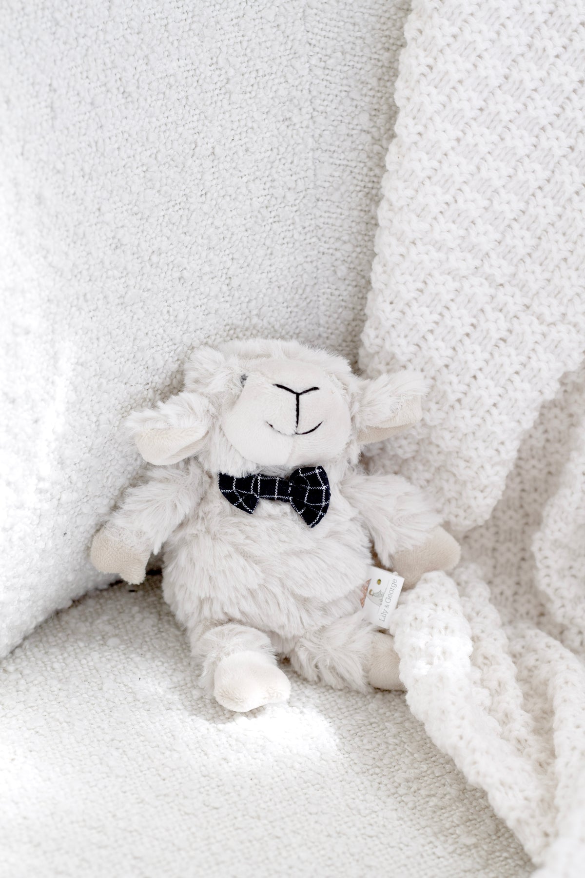 Liam the Lamb rattle sitting on a white textured throw
