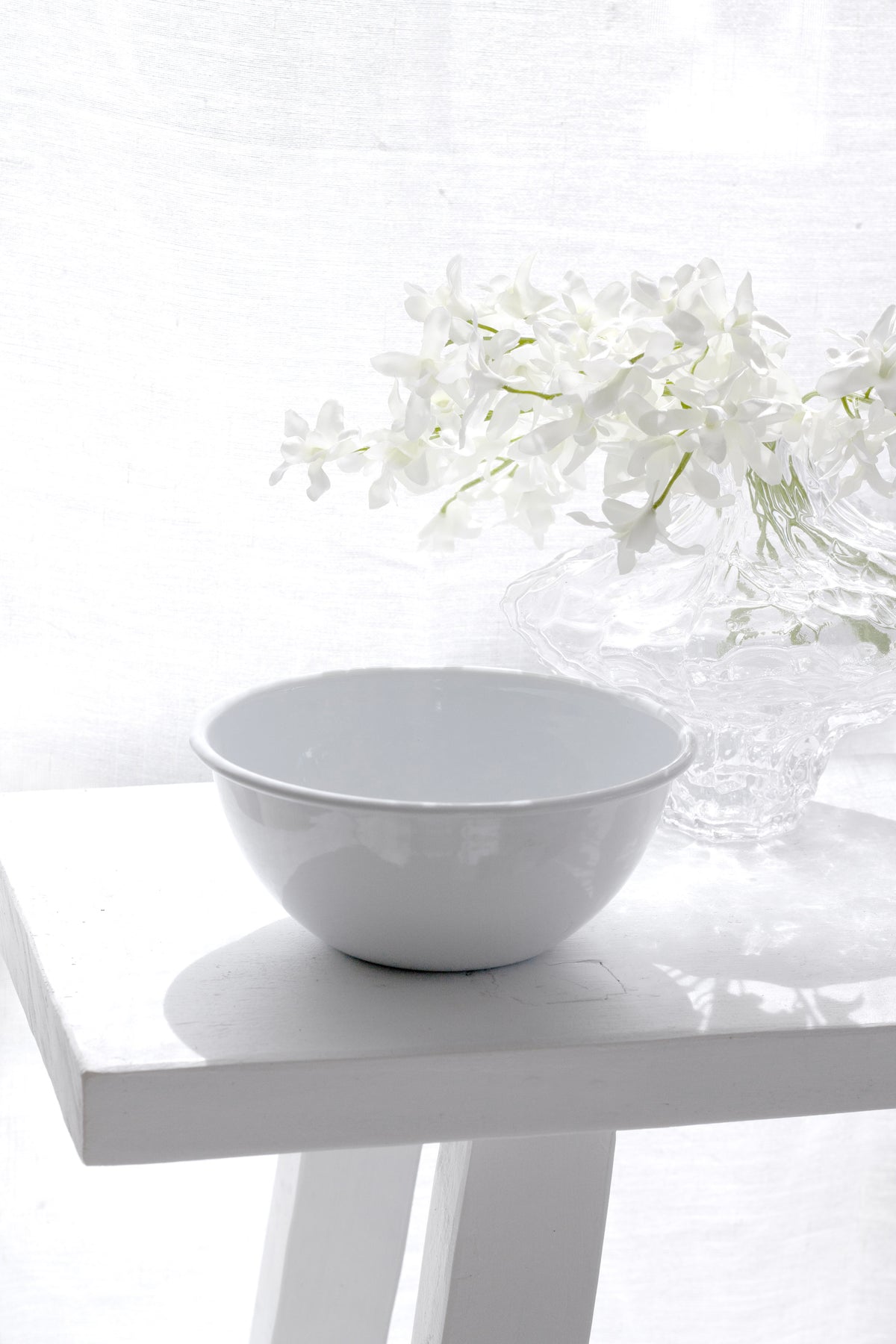 White enamel noodle bowl on a white plinth with flowers alongside