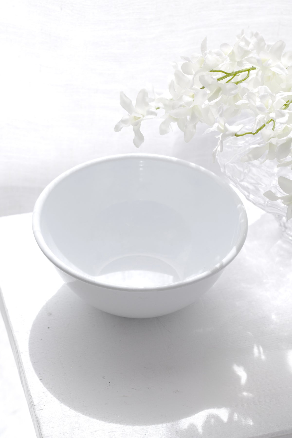 White enamel noodle bowl on a pale surface with white flowers behind