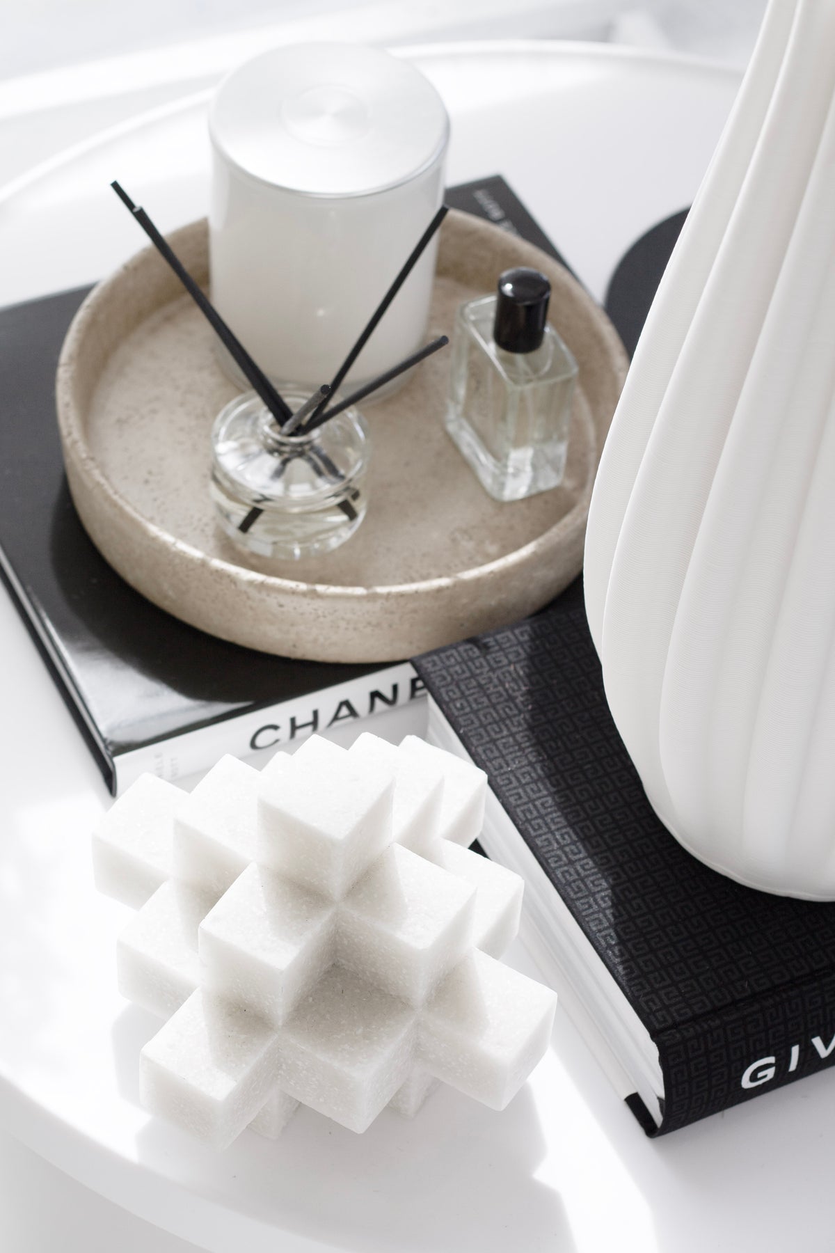 White Cubism sculpture on a shelf beside a reed diffuser and stacked books