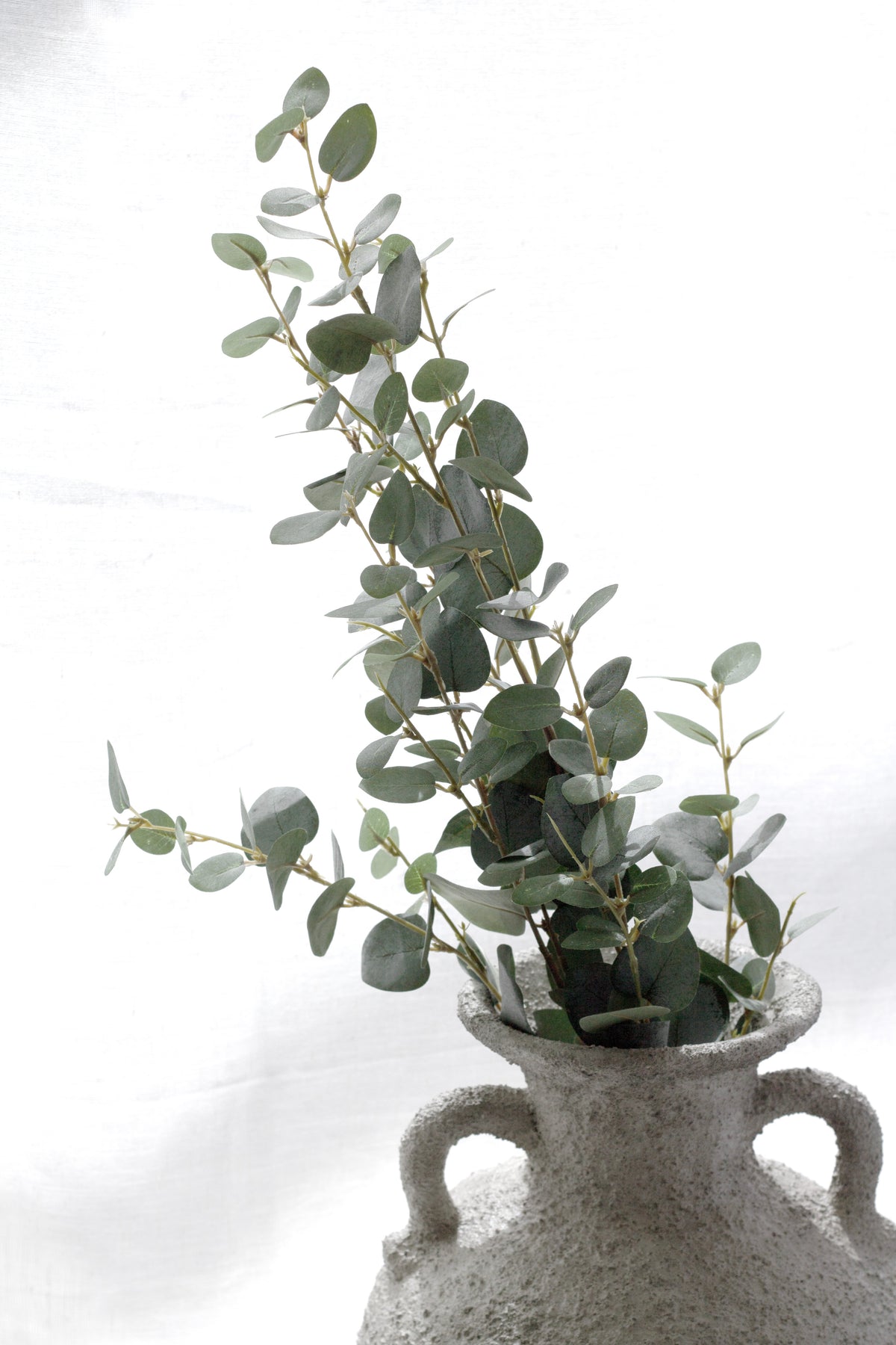 Faux eucalyptus stems in a grey stone urn with handles