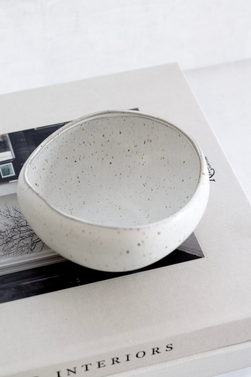 Speckled gray ceramic bowl on top of a book titled 'Interiors' with a white background