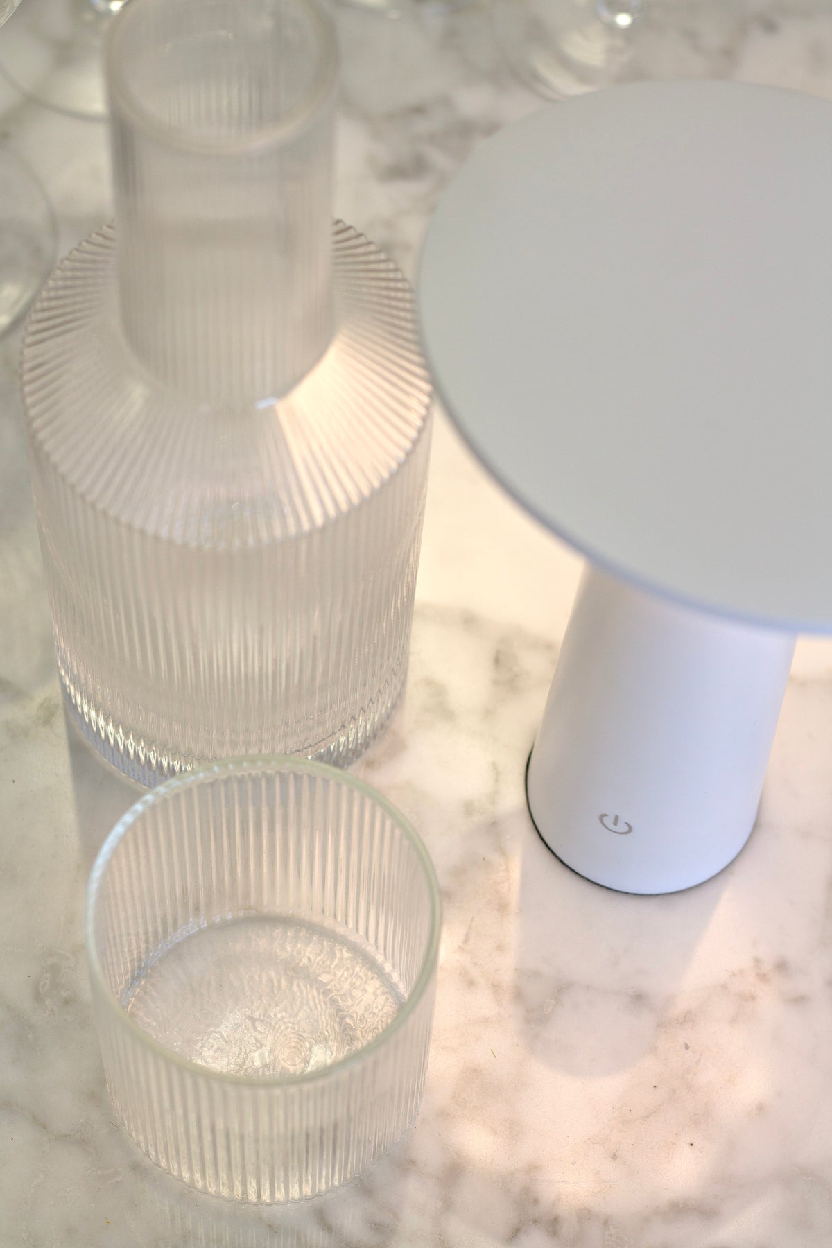 Close view of a ribbed glass carafe and tumbler beside the white LED Tilt lamp