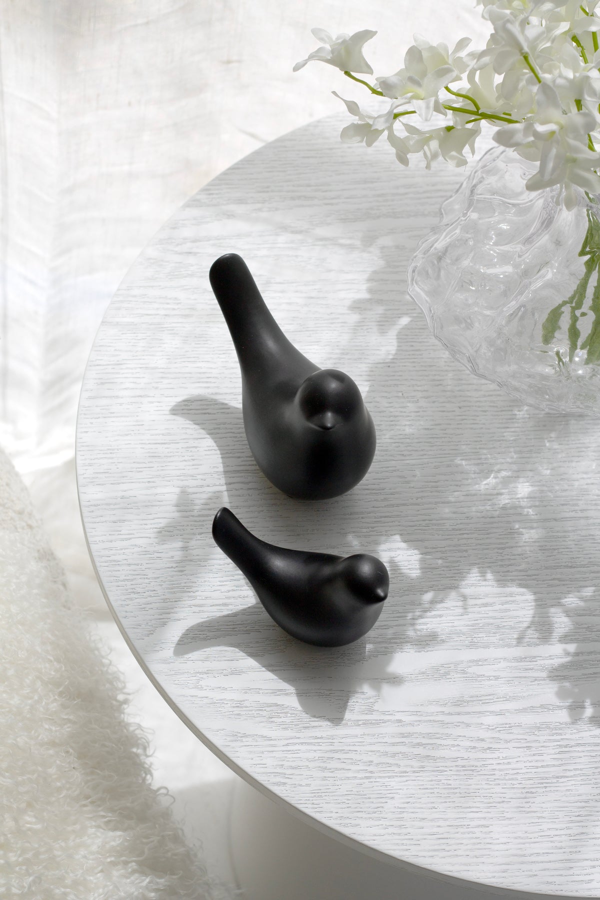 Two black Della ceramic doves on a round table beside white flowers