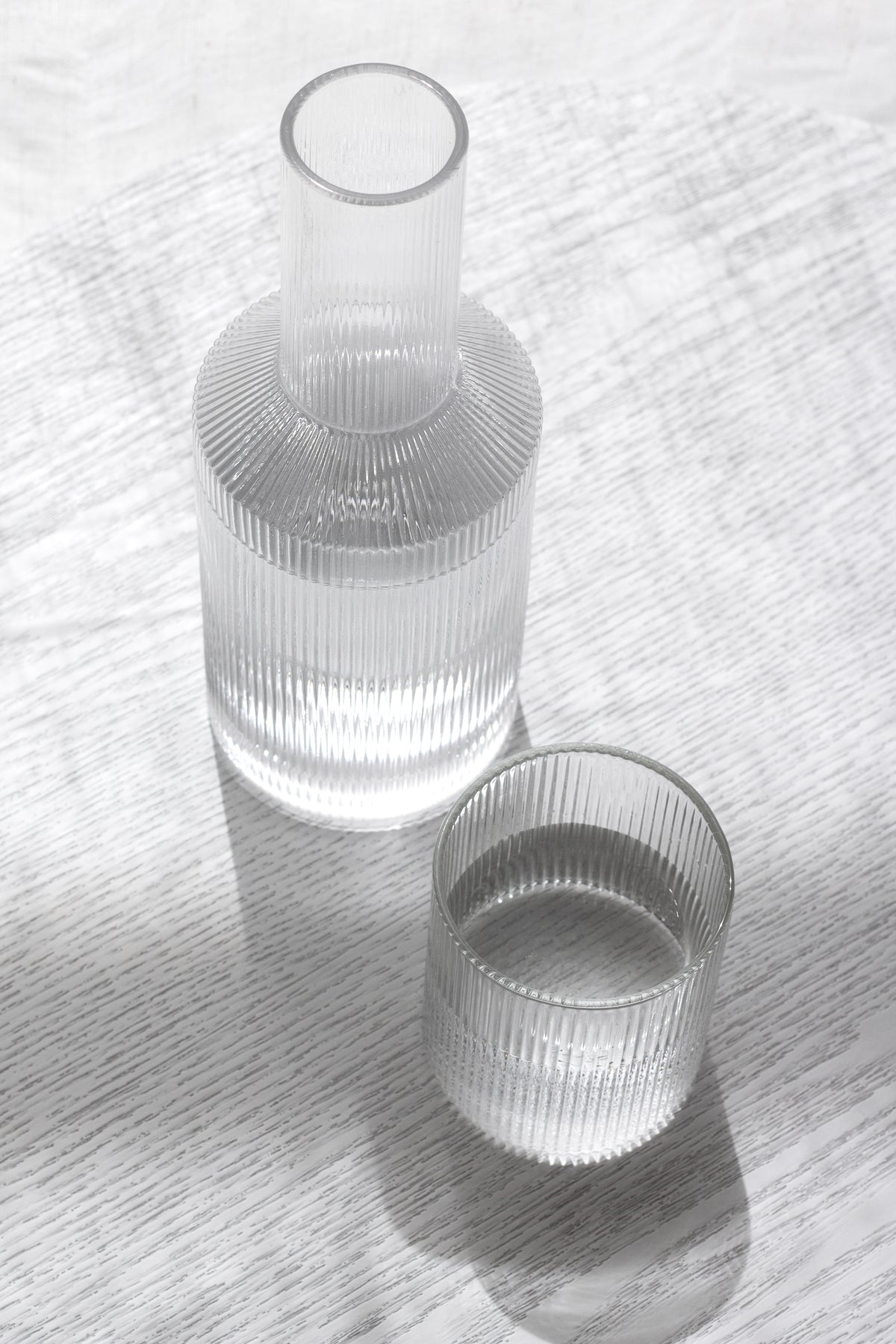 Amalfi decanter and fluted glass casting soft shadows on white linen