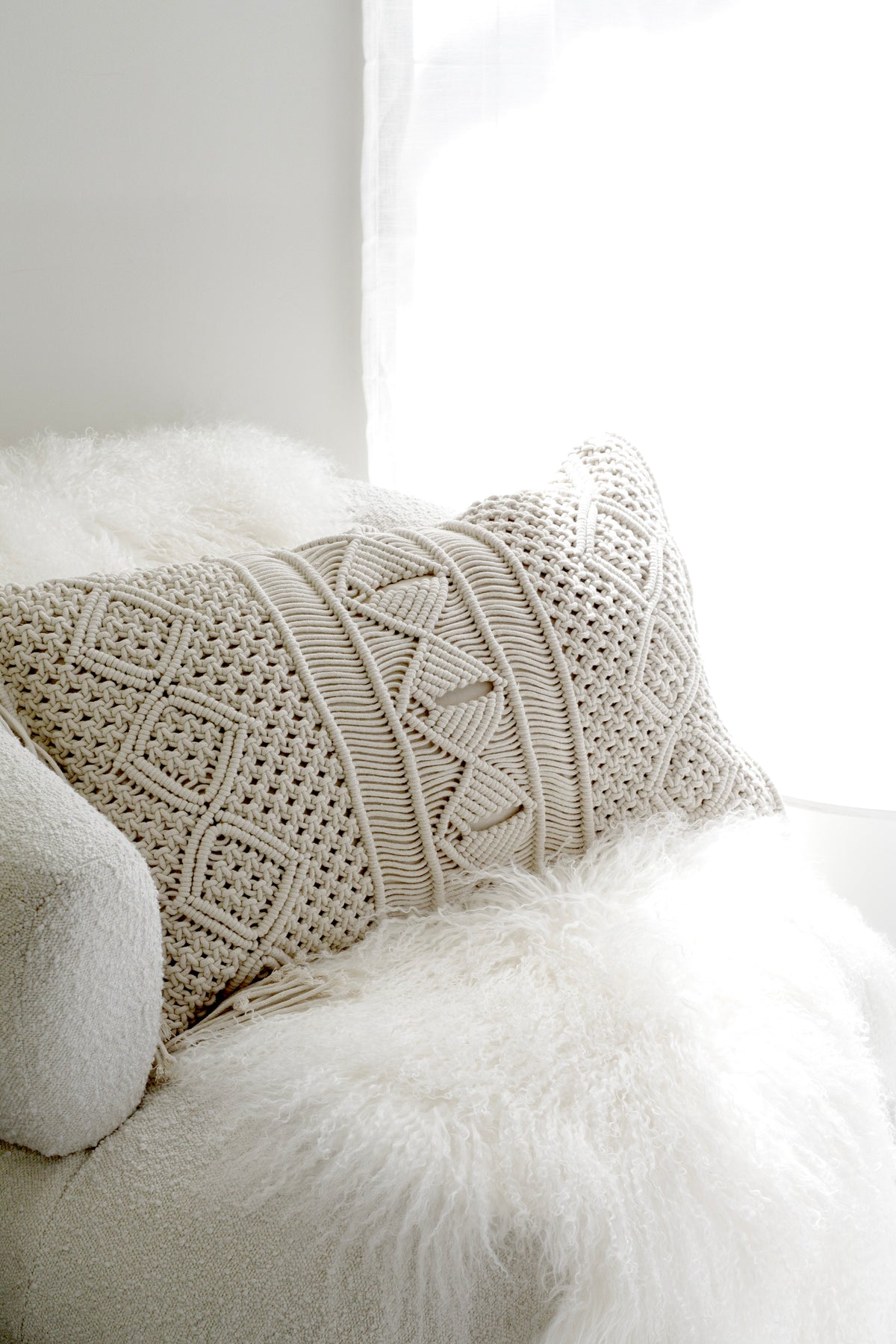 Macrame cushion resting on a white sheepskin in bright window light
