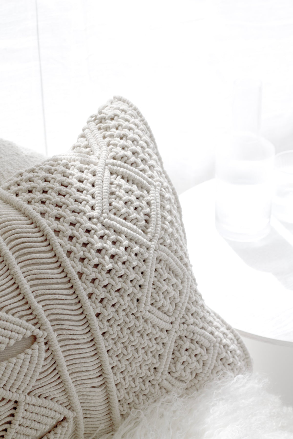Corner of the macrame cushion on a sheepskin, the knotted diamond pattern in close view