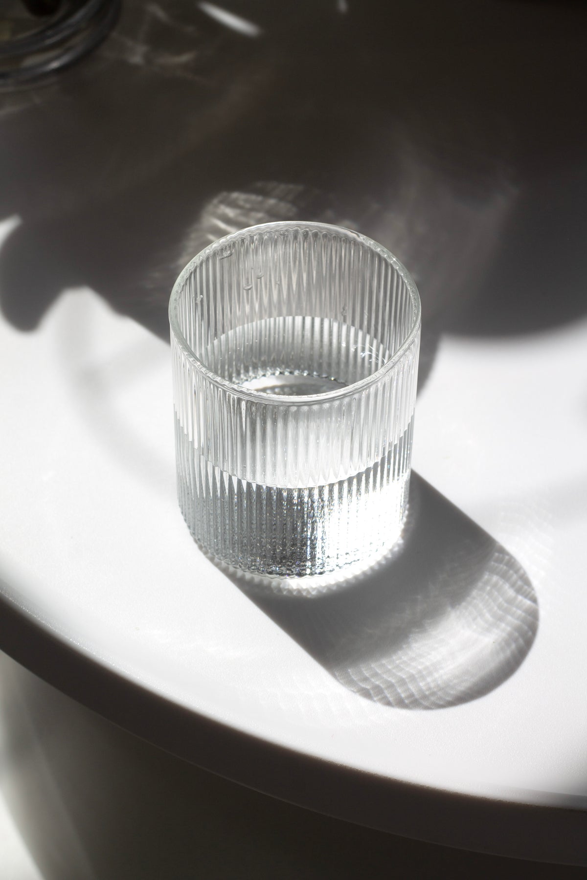 Fluted water glass in bright sunlight casting a ribbed shadow on a dark surface