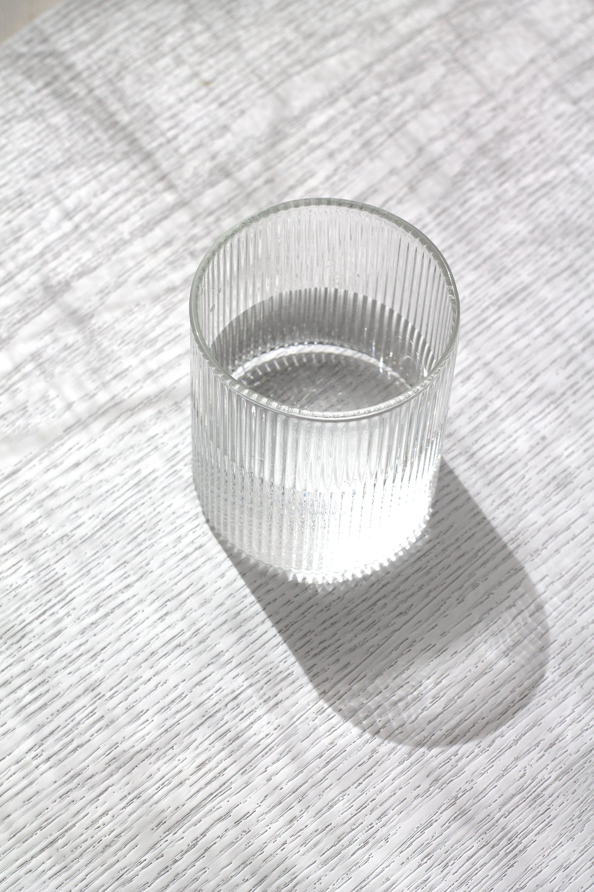 Top-down view of a fluted water glass and its shadow on white linen