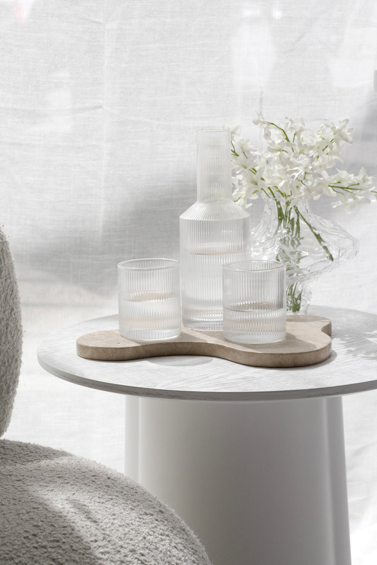 Amalfi decanter with white flowers and glasses on a tray beside a boucle chair