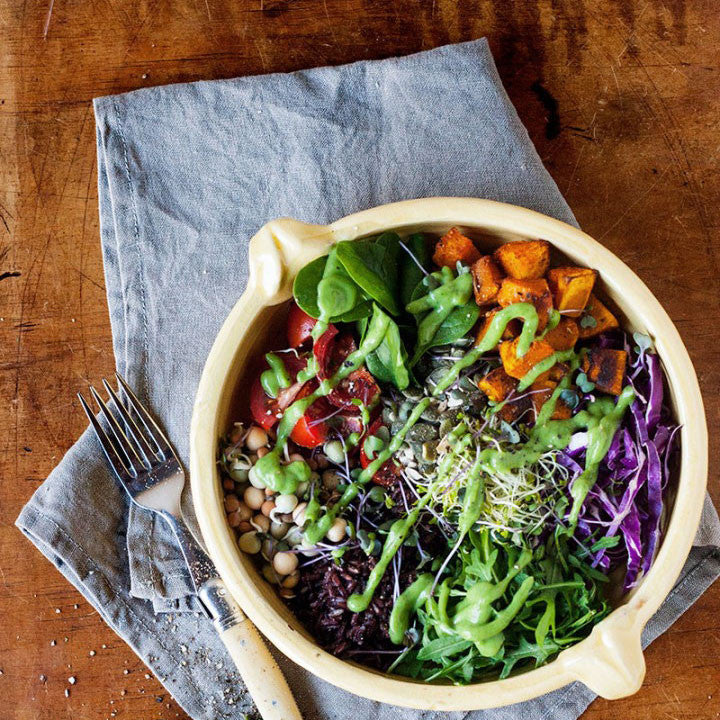 Salad bowl of chickpeas, sprouts, greens and roasted kumara with green dressing on a wooden table