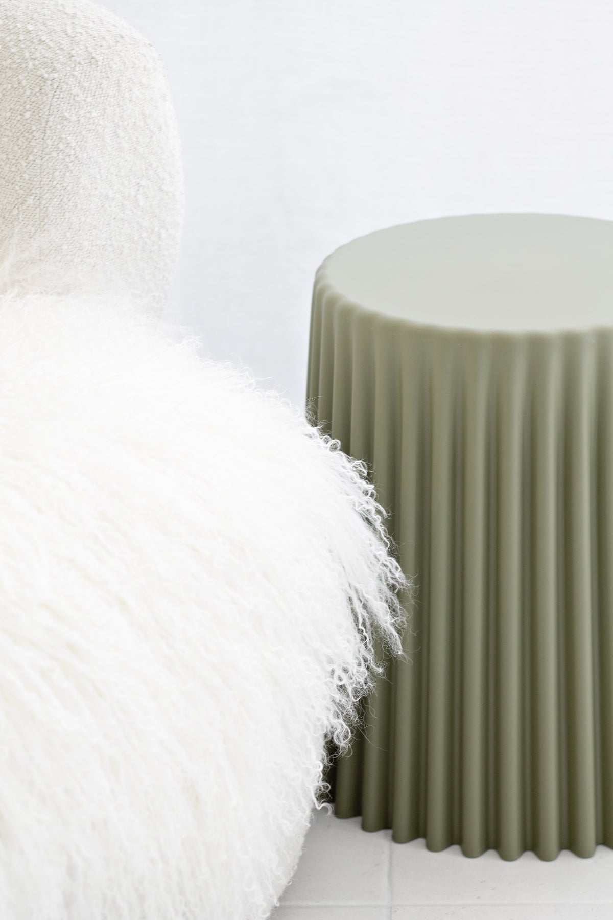 Olive ribbed stool beside a white boucle chair with a soft white cushion