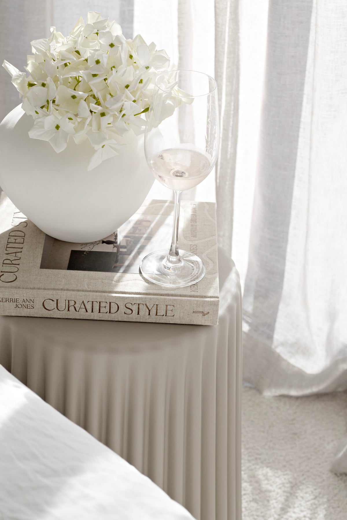 Nude ribbed stool holding a rounded white vase of hydrangeas, a wine glass and books