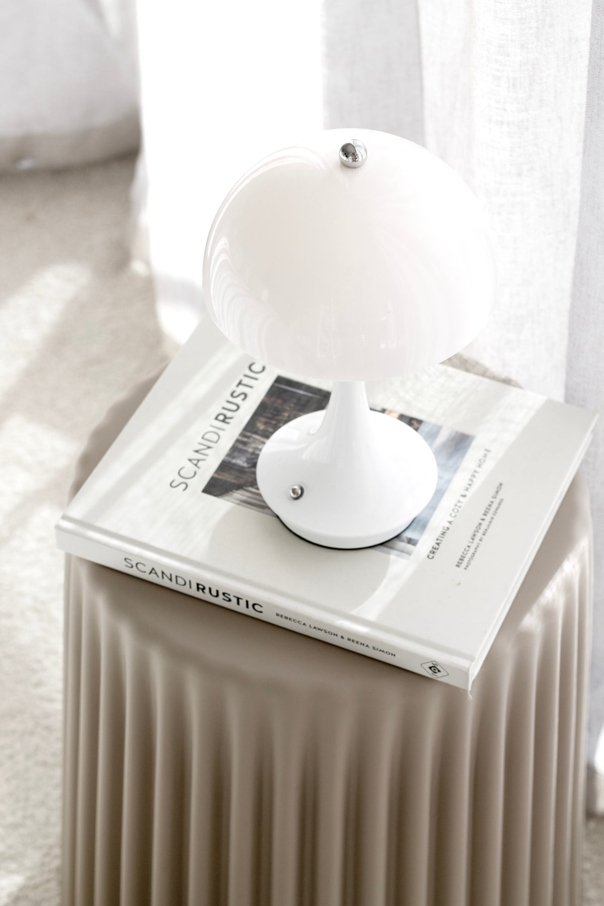 White mushroom lamp unlit on stacked books on a fluted bedside table