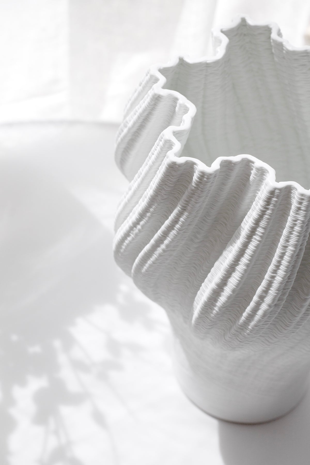 Close view of the pleated vase rim, the ridged folds lit by bright window light
