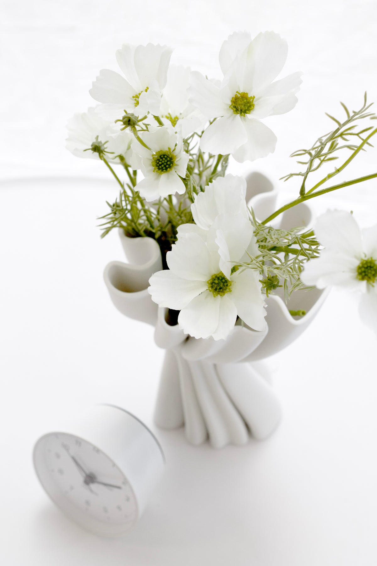 White Cooper 3D printed vase holding white cosmos flowers beside a small round clock