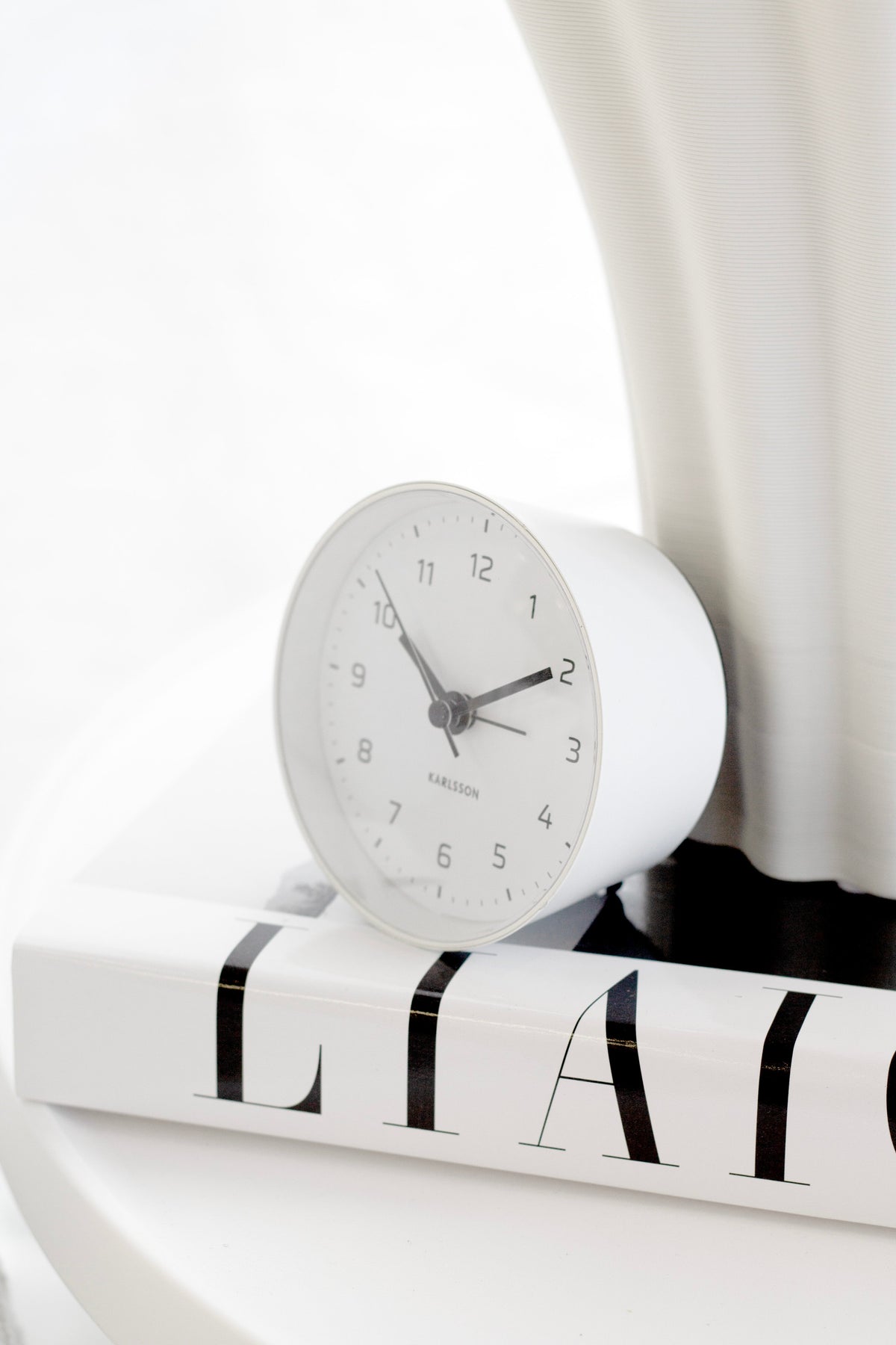 White Cone alarm clock on a stack of books beside a white wavy vase