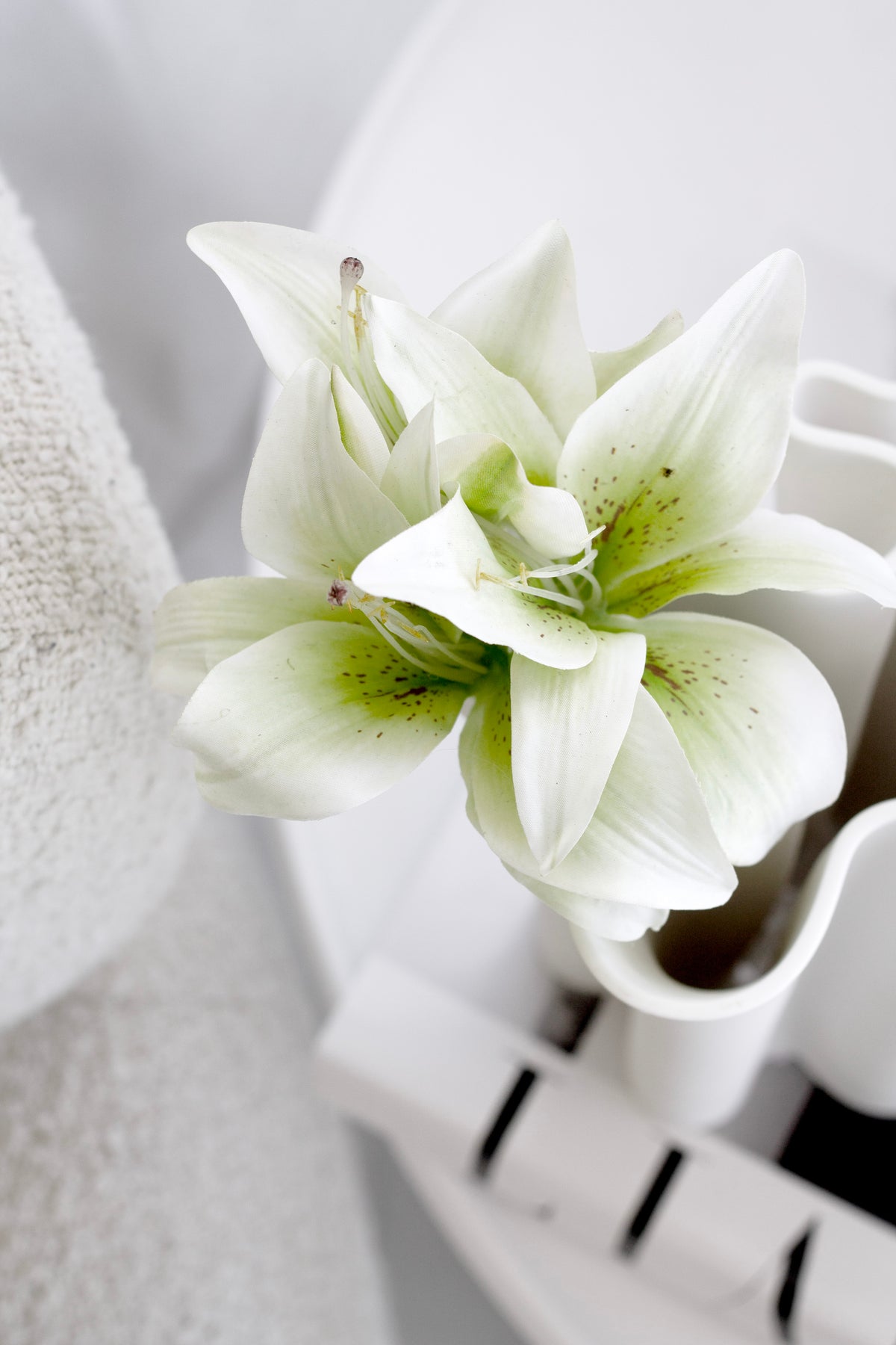 Close view of a cream lily with a green throat in a white vase by a curtain