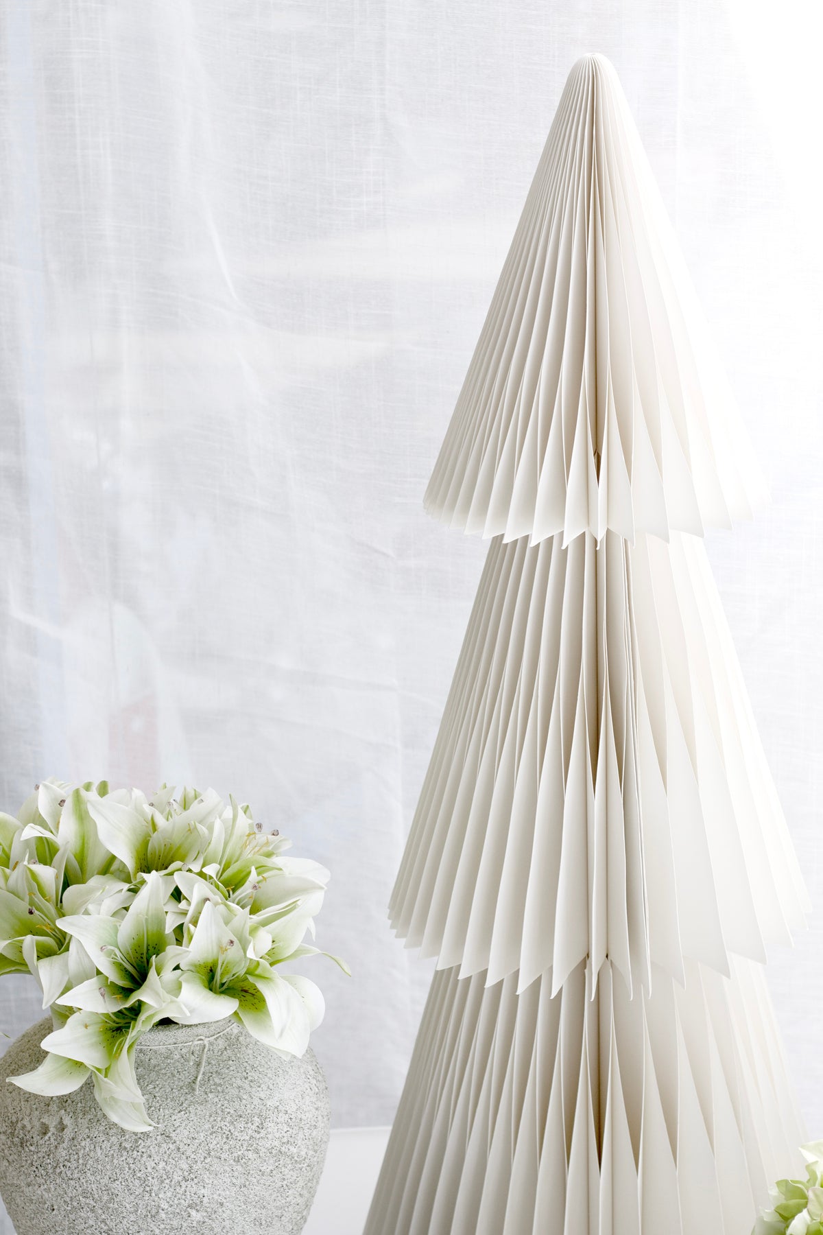 Small vase of cream lilies beside a tall pleated paper tree