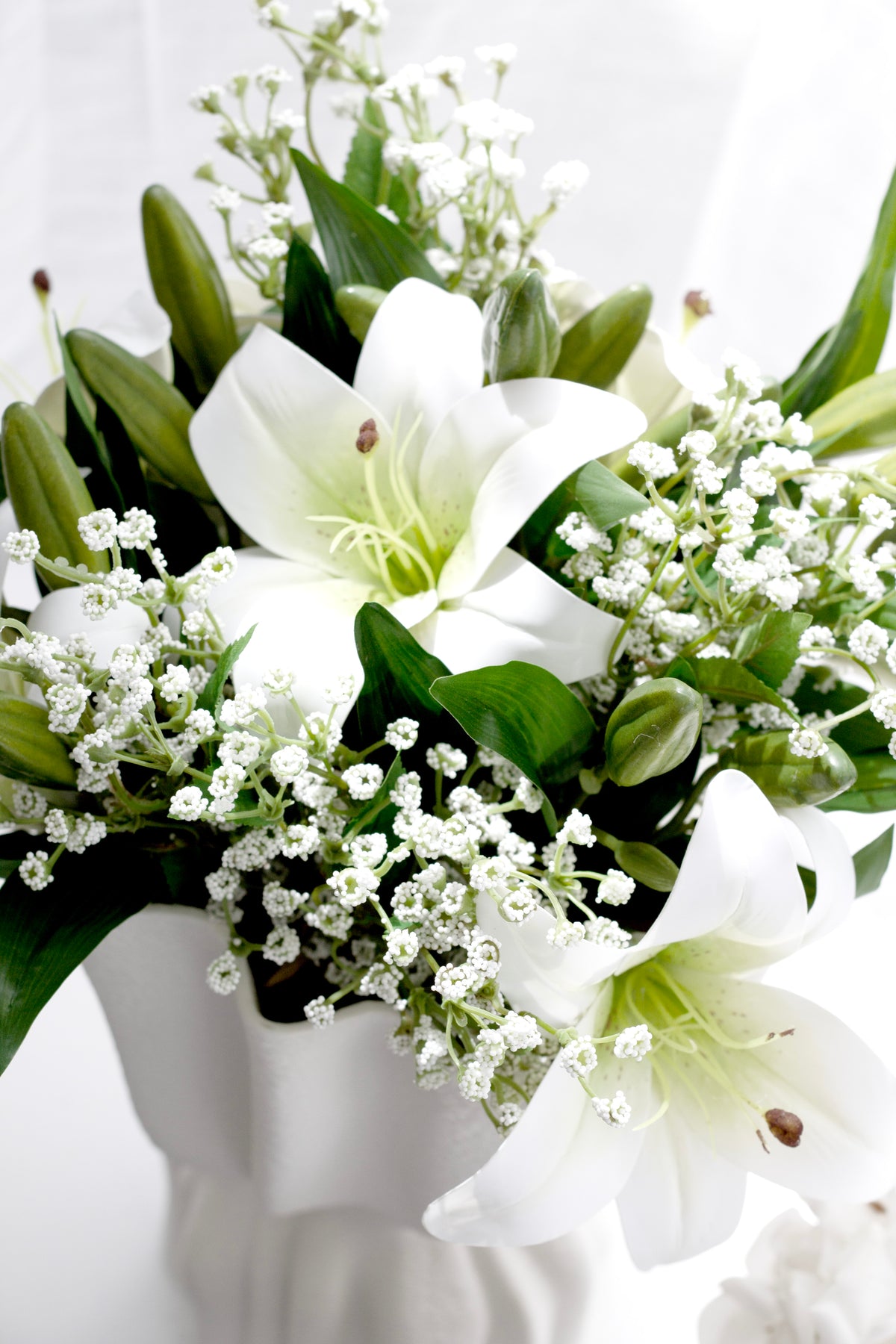 Close view of white lilies and baby's breath in a ruffled vase