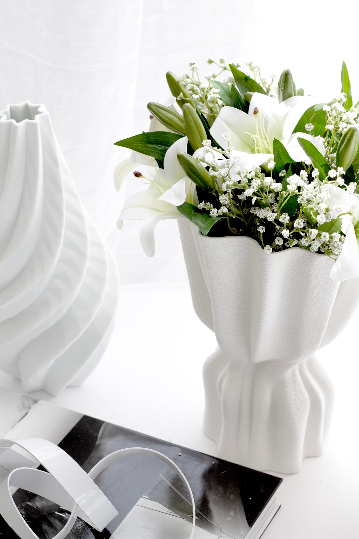 White market lilies with gypsophila arranged in a fluted white vase