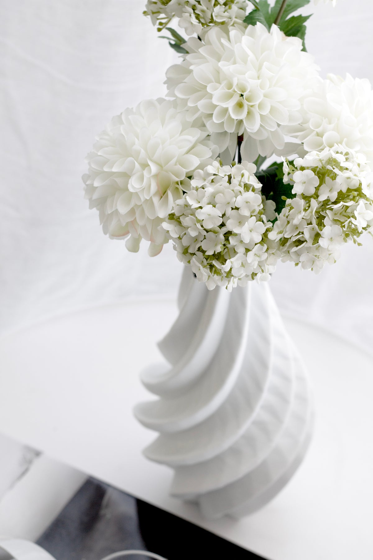 White viburnum arranged in a fluted white vase, foliage spilling to the side