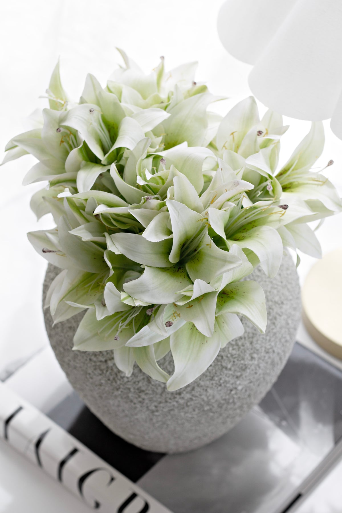 Cream lily bundle in a speckled stone vase resting on a hardback book