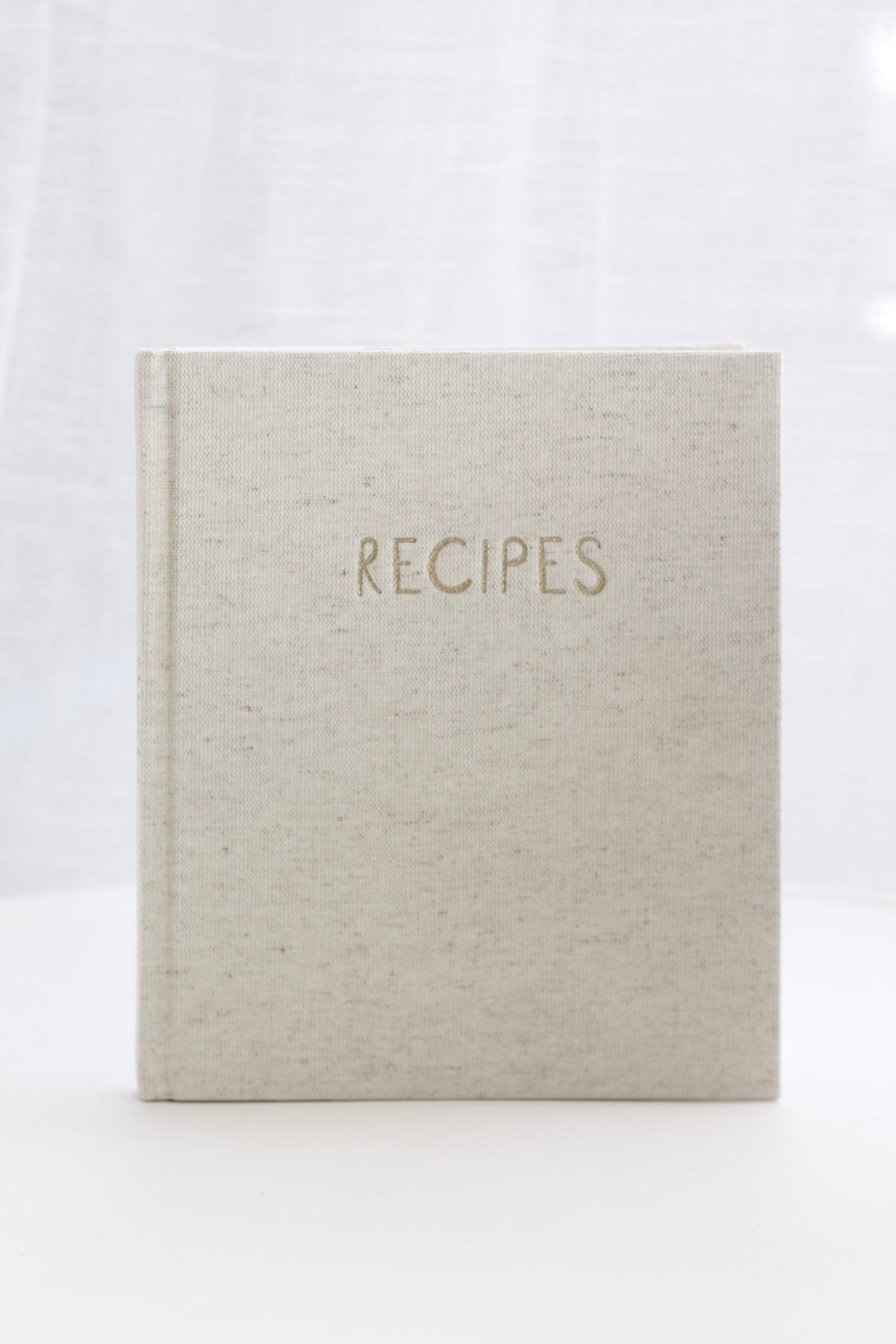 Oatmeal linen recipe journal styled upright showing the embossed cover and spine