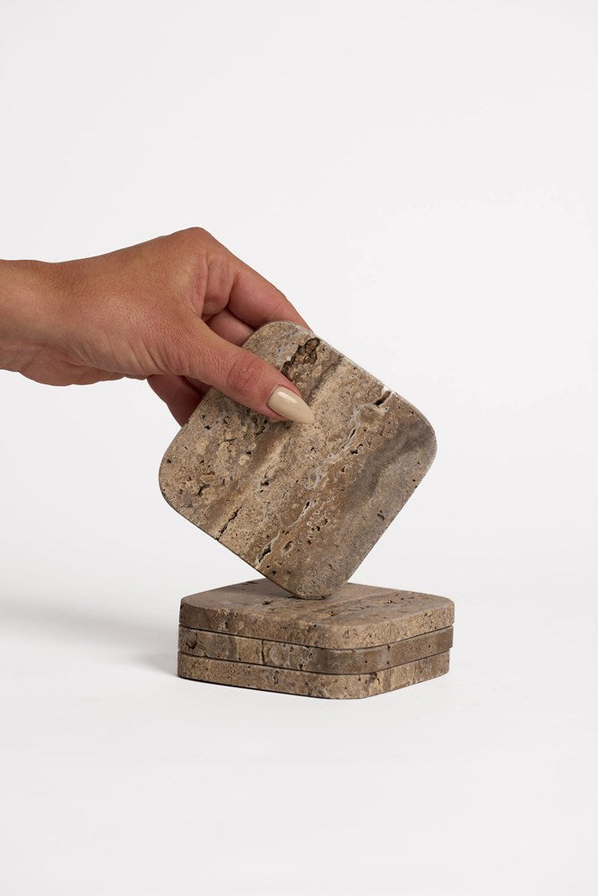 Hand lifting a travertine coaster from a stack of stone coasters