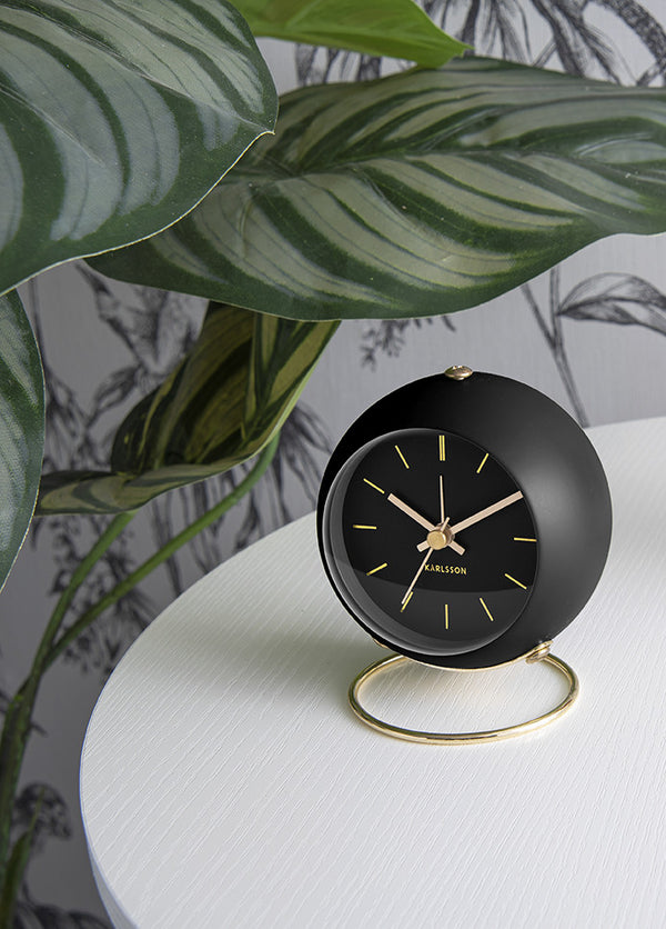 Black Globe alarm clock on a white table in front of large striped leaves