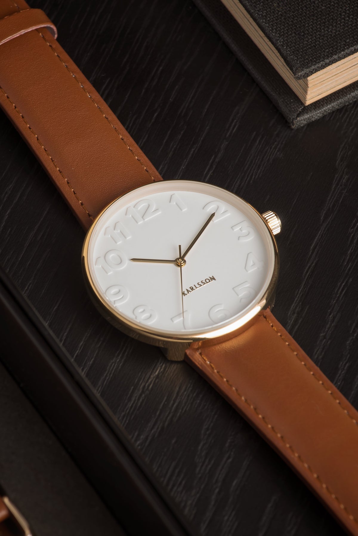 Close up of the Karlsson Mr White Steel watch face and tan strap on a dark wood surface