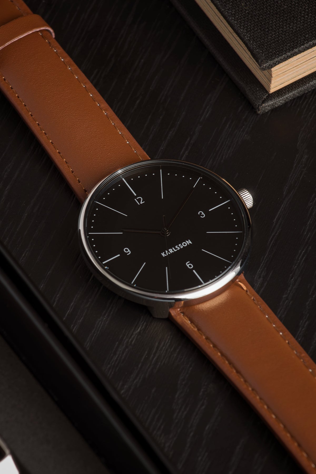 Close up of the Karlsson Normann black dial and tan strap on a dark wood surface