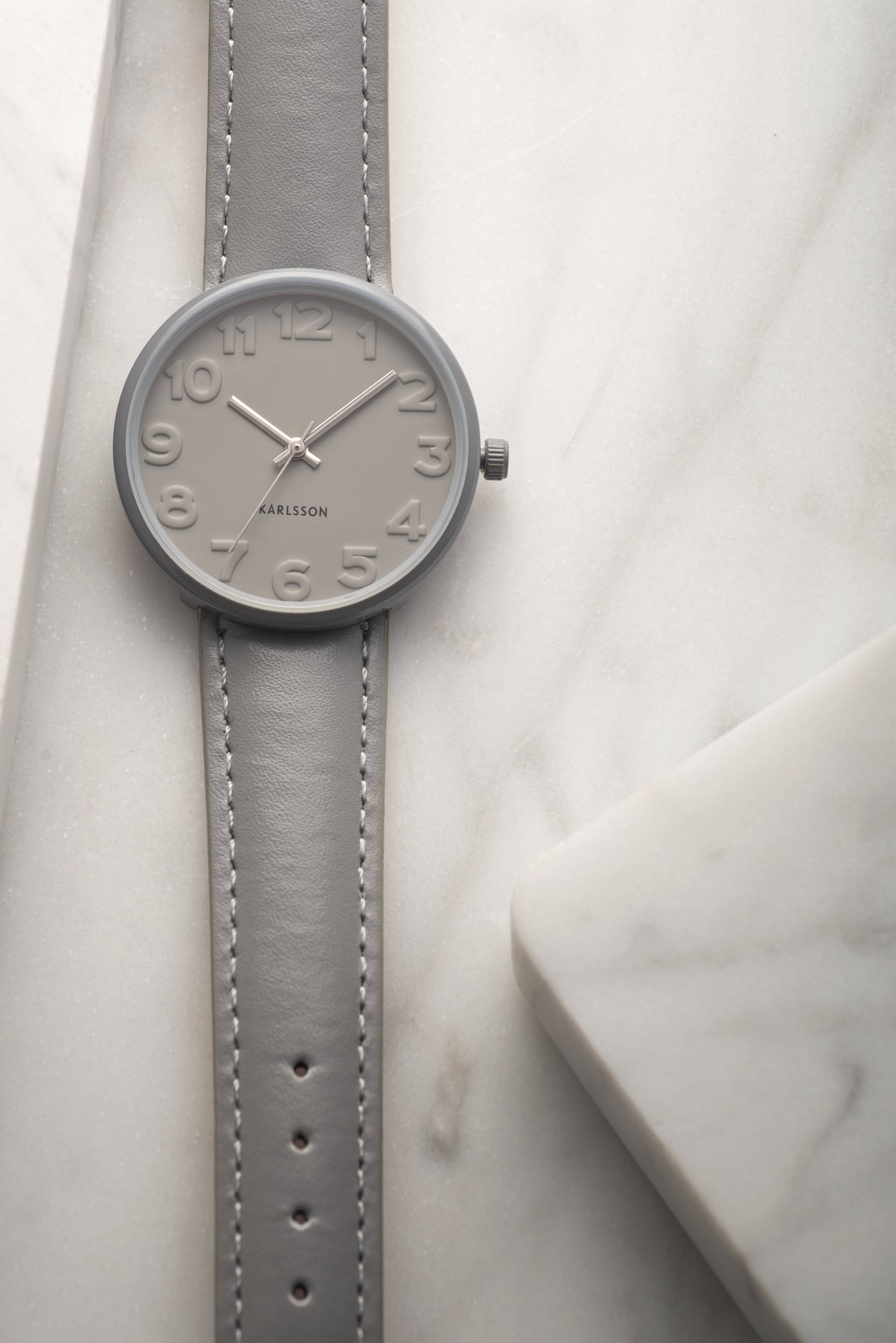 Close up of the Karlsson Ms Grey watch face and raised numerals on white marble