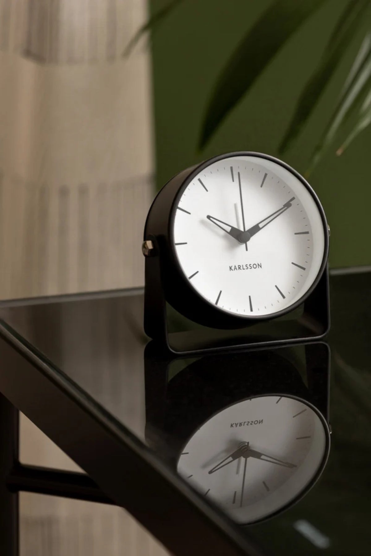 Black Karlsson Calm alarm clock on a black glass side table beside a plant