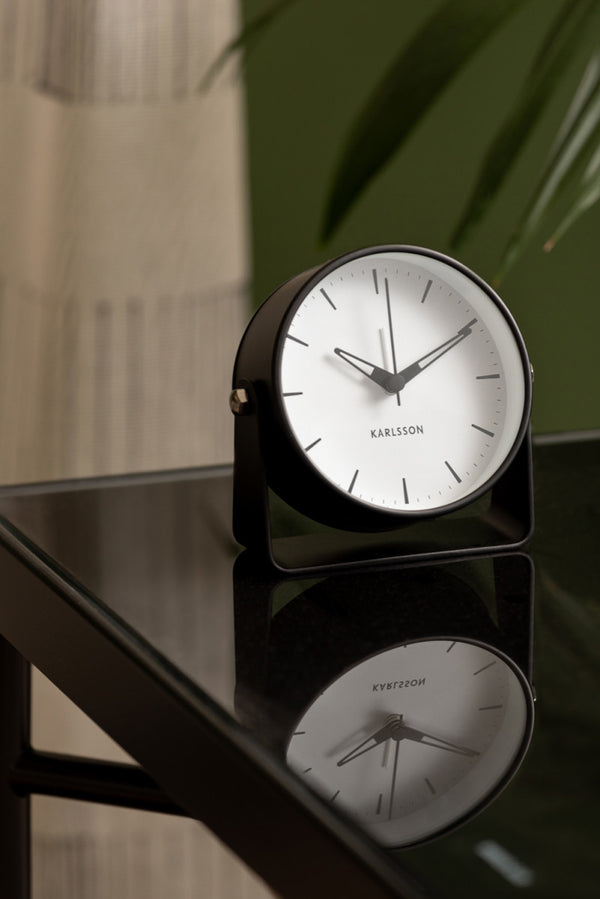 Black Karlsson Calm alarm clock on a black glass side table beside a plant