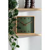Dark green Nervadura wooden wall clock styled on a shelf with greenery