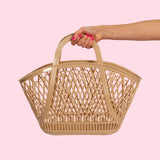 A hand holding a recyclable Sun Jellies Betty Basket on a feminine pink background.