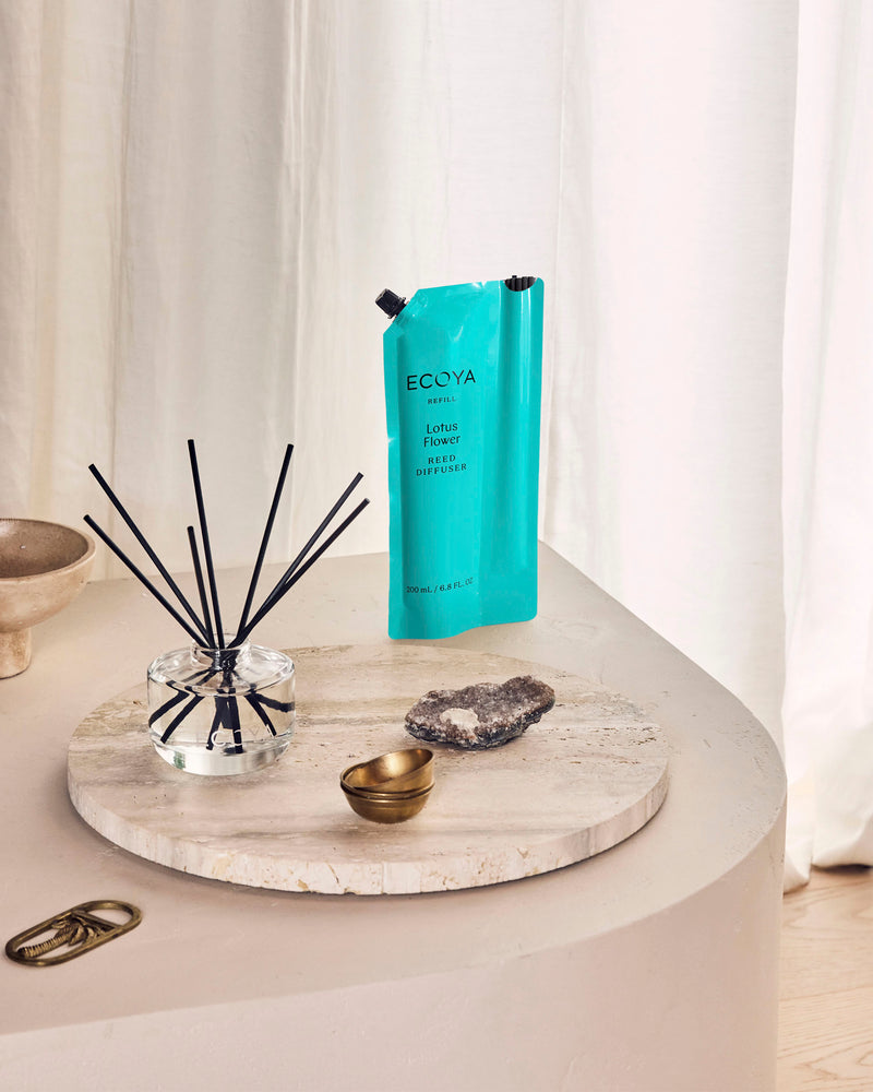 Ecoya Lotus Flower reed diffuser with its teal refill pouch on a travertine tray