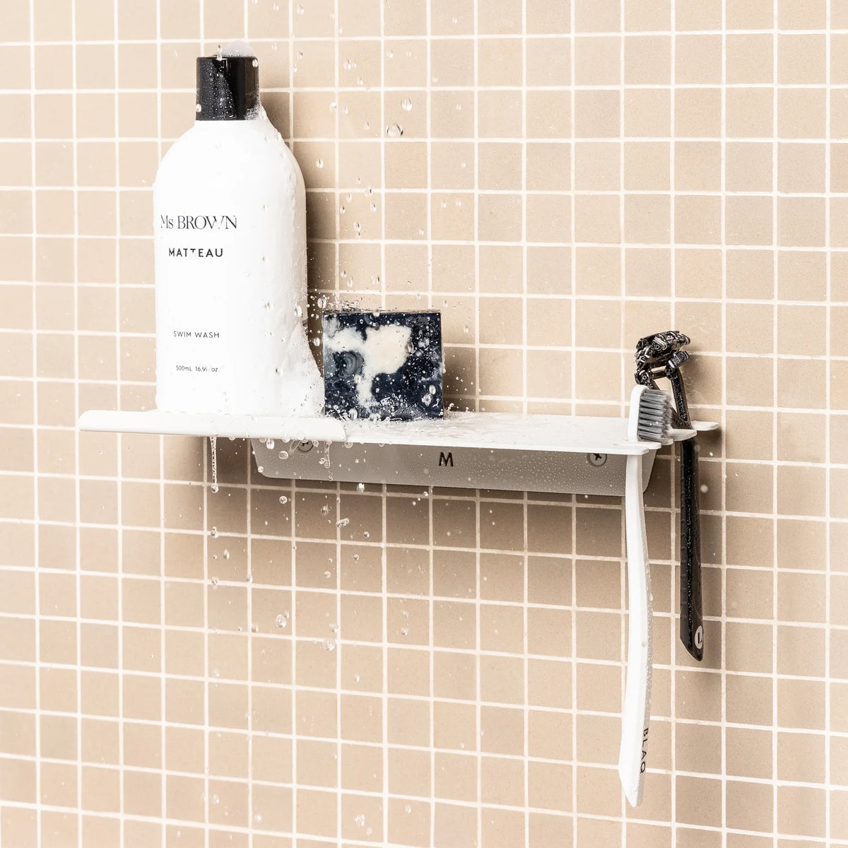 White FOLD shower shelf with bottles and a toothbrush on blush pink tiles