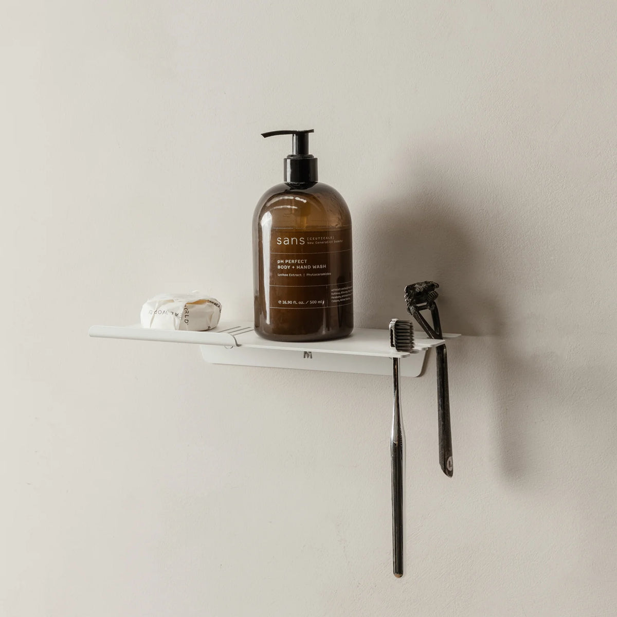 White FOLD shower shelf with an amber bottle, razor and toothbrush on a grey wall