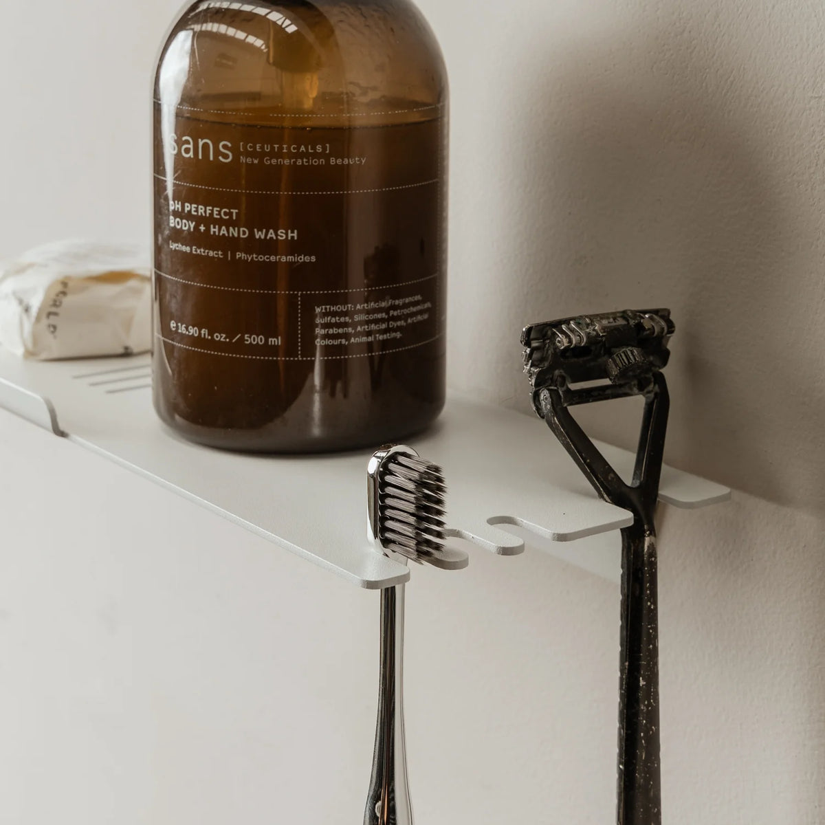 Close view of the white FOLD shower shelf with an amber bottle and razor